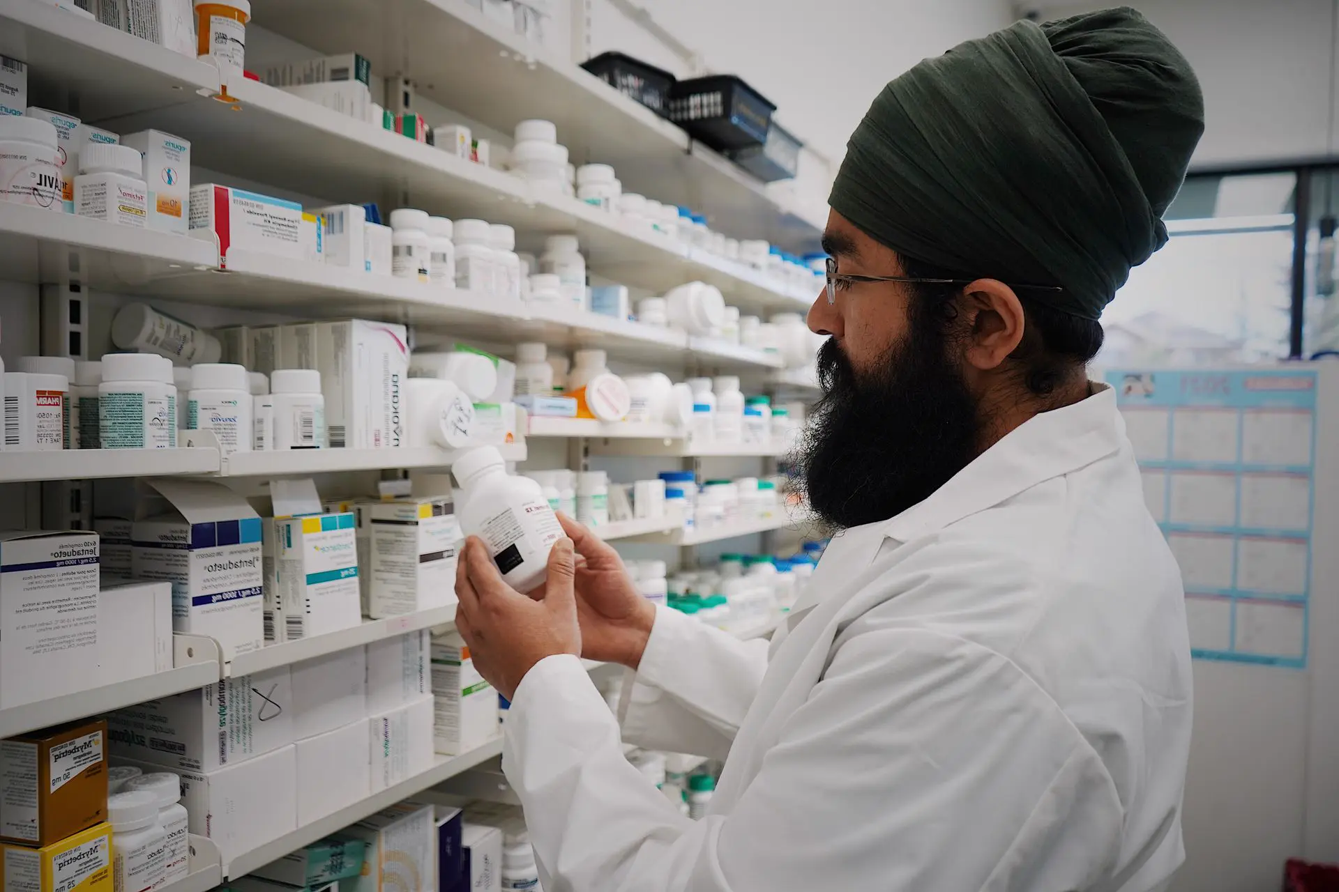 Pharmacist in a white coat checking a medicine bottle in a pharmacy