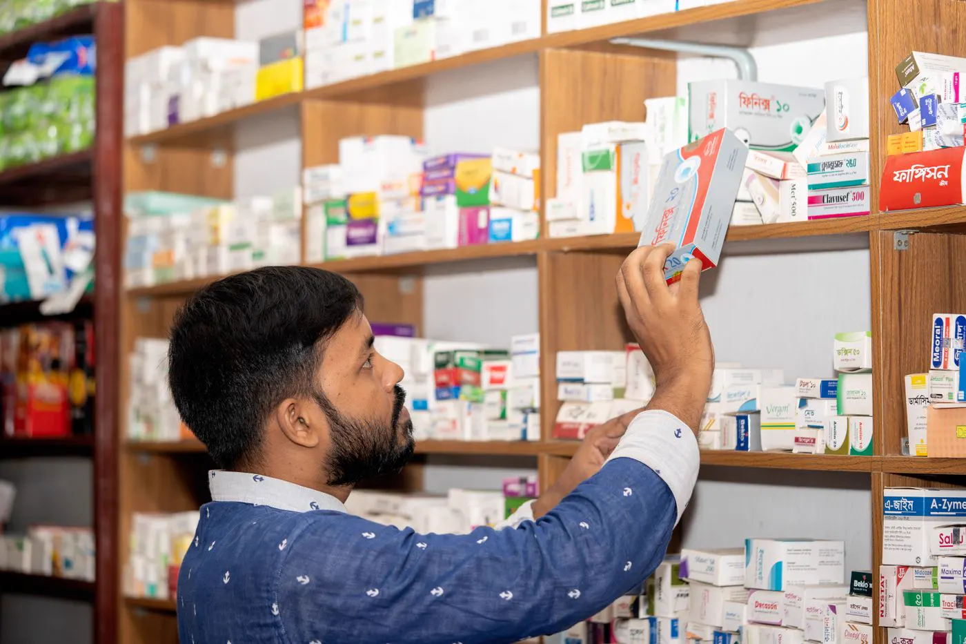 Pharmacist taking a medicine box from a stocked pharmacy shelf