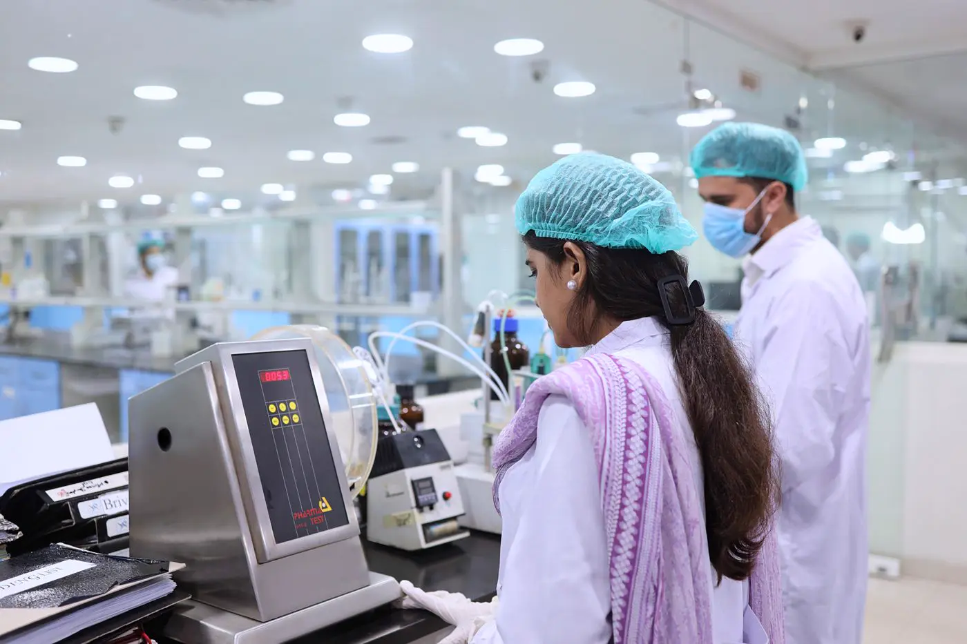 Quality control staff in hairnets testing samples in a pharmaceutical laboratory